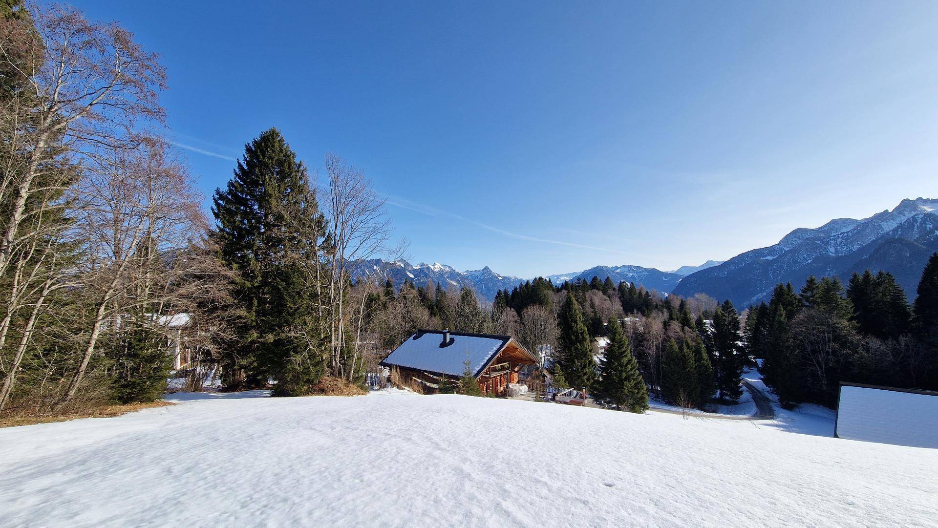 Charmantes Holzhaus in verschneiter Umgebung mit weitem Blick auf die umliegende Berglandschaft.
