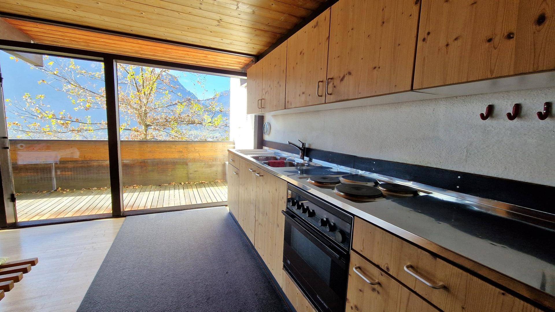 Helle Küche mit Holzfronten, Edelstahl-Arbeitsplatte und weitem Bergblick durch große Fenster.
