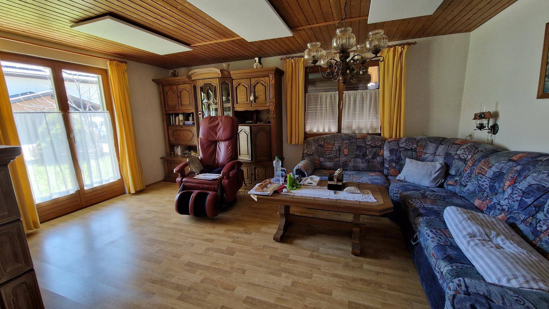 Wohnzimmer mit Holzdecke, traditionellen Möbeln und Zugang zu einem Außenbereich durch große Fenster.
