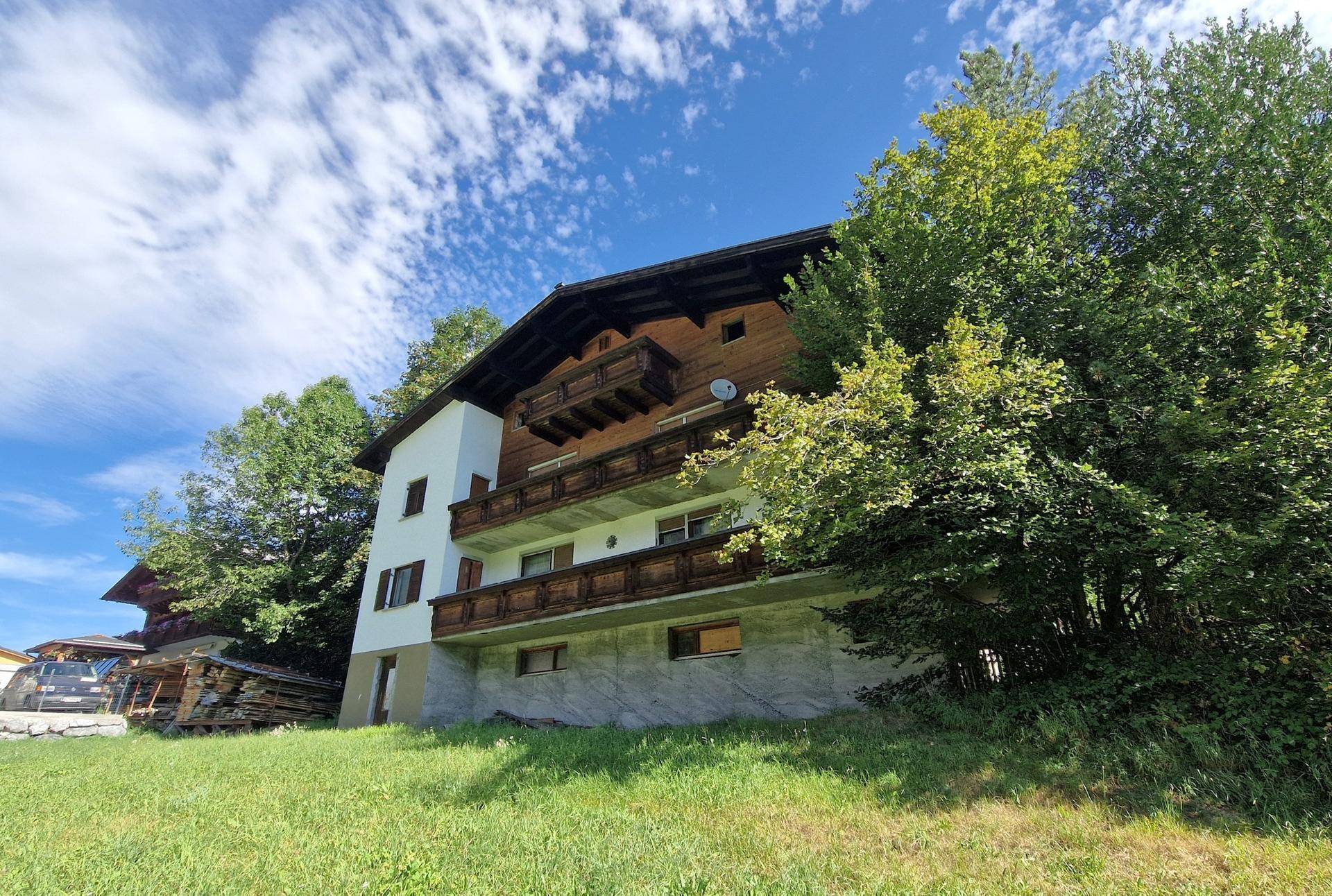 Detailansicht des Hauses mit Holzbalkonen und weißer Fassade unter blauem Himmel und Bäumen.