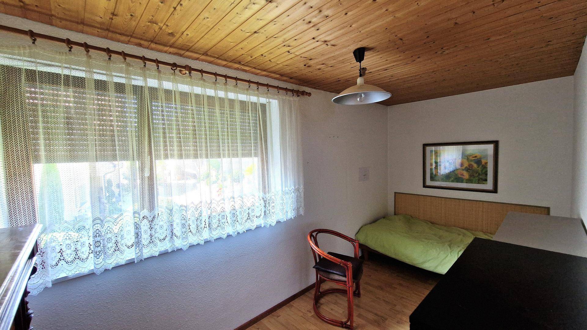 Helles Schlafzimmer mit Holzdecke, Holzboden und einem großen Fenster mit Rollläden.