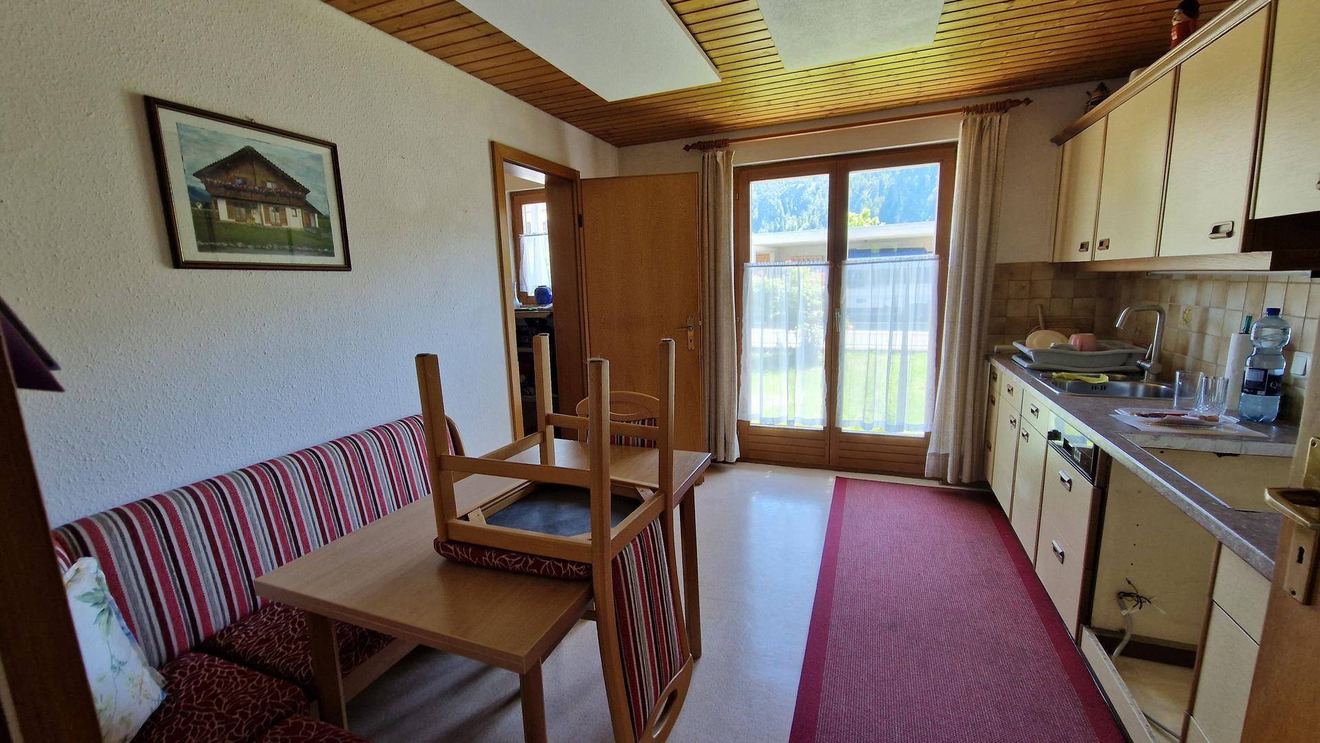 Funktionale Küche mit Holzschränken, Essbereich und großem Fenster mit Blick ins Grüne.