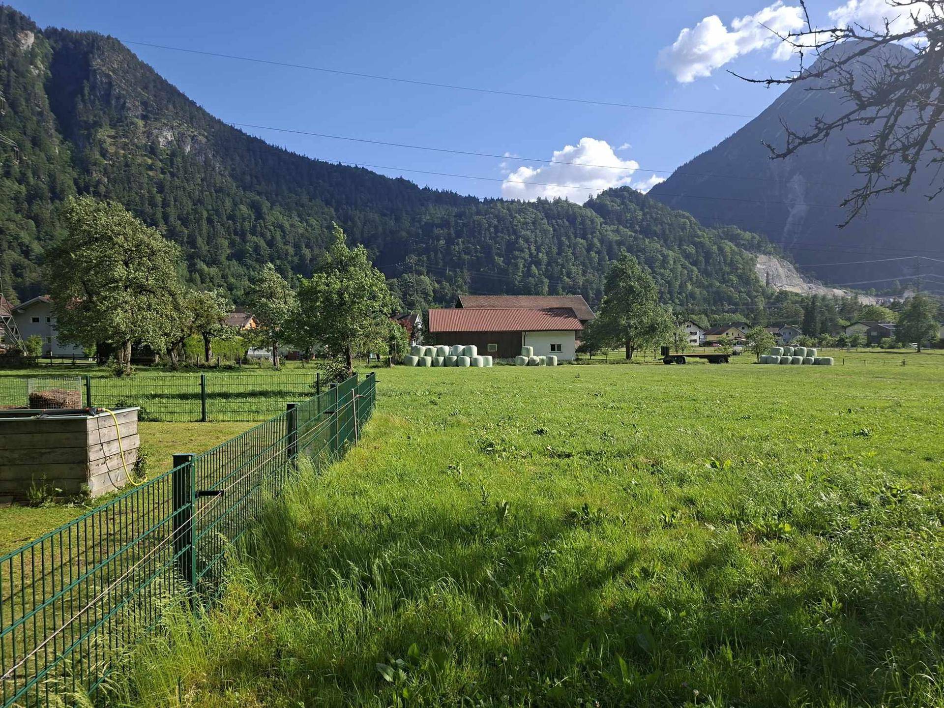 Idyllische Landschaft mit grünen Feldern, Bergen im Hintergrund und einem Bauernhof in der Ferne.