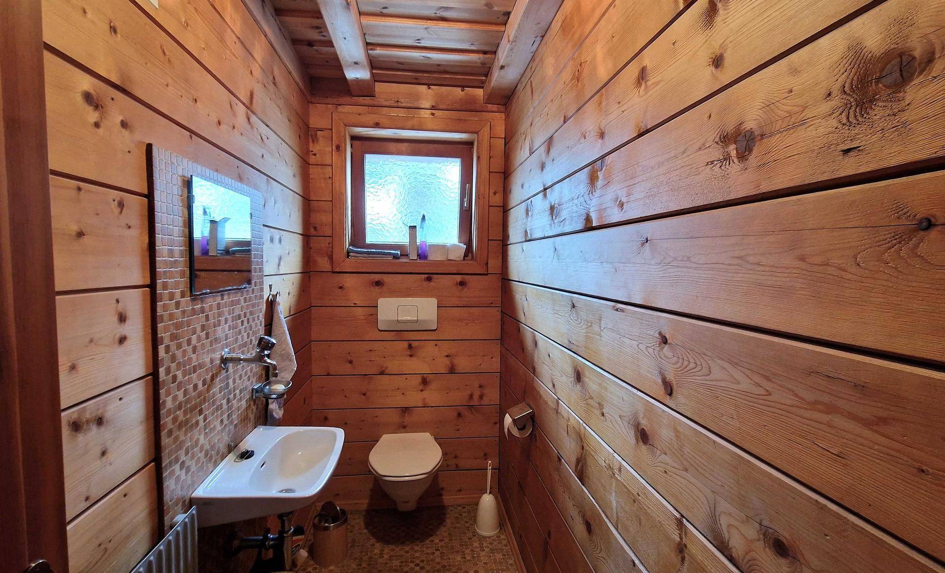 Kleines WC mit Holzvertäfelung, Waschbecken und Fenster.