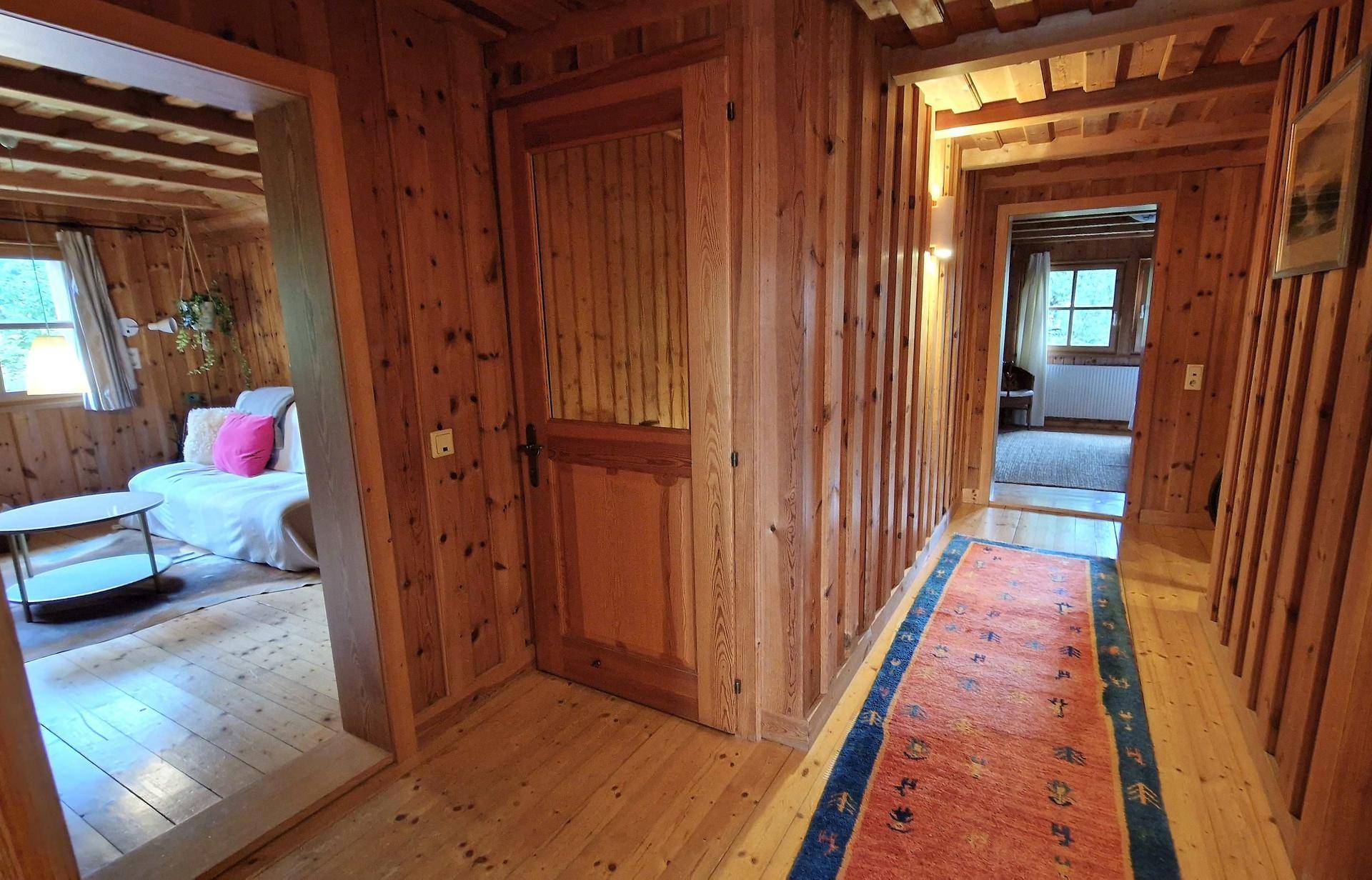 Langer Flur mit Holzboden, Holzvertäfelung und einem bunten Teppich.