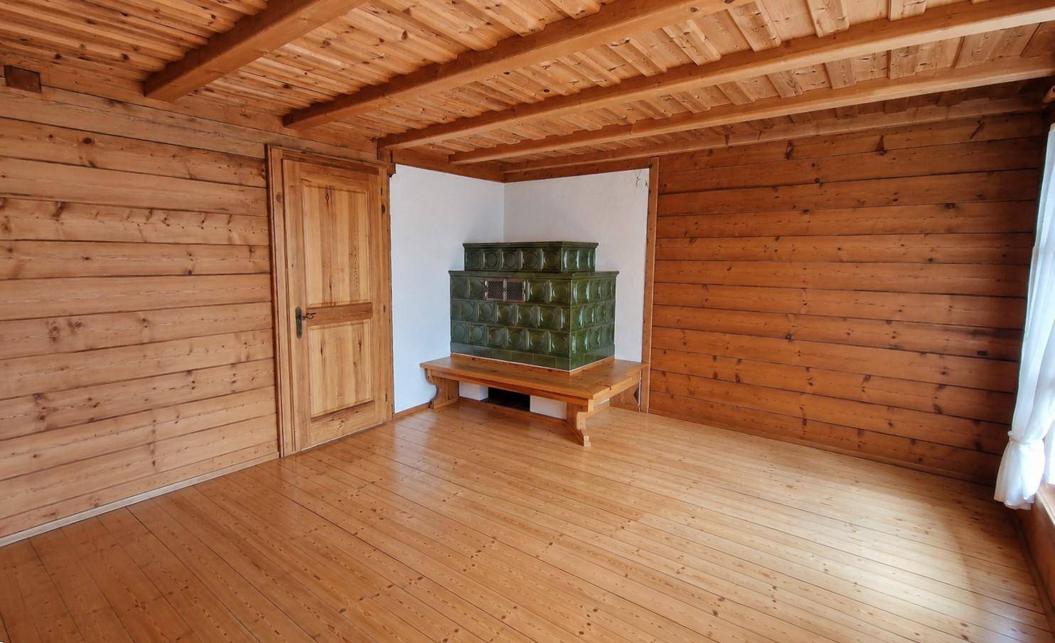 Gemütlicher Raum mit Holzboden, Holzvertäfelung und einem traditionellen grünen Kachelofen.