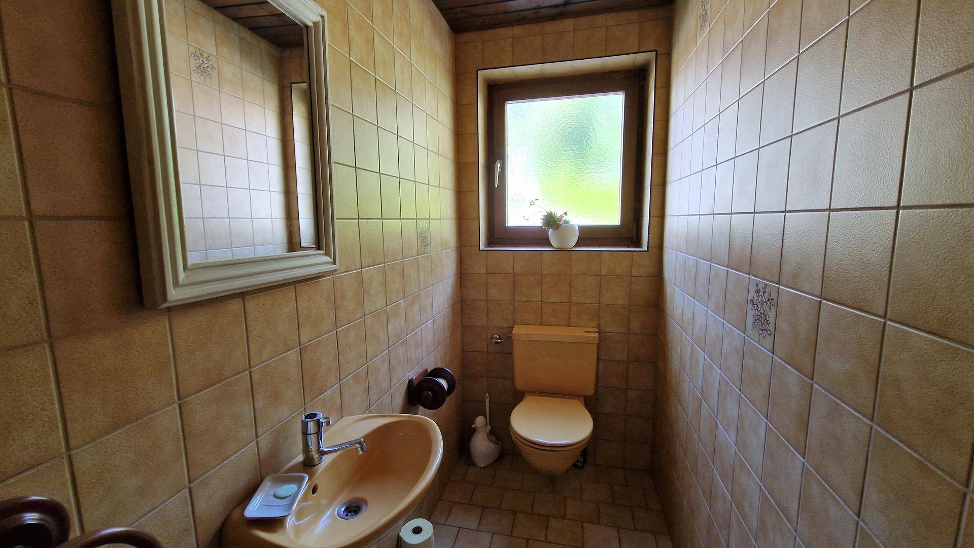 Kleines Gäste-WC mit beigefarbenen Fliesen, Fenster und einfacher Ausstattung.
