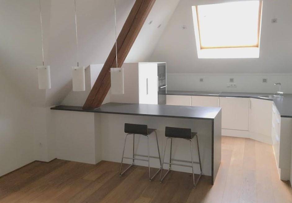 Moderne Küche im Dachgeschoss mit Kochinsel, Holzbalken und viel Tageslicht durch Dachfenster.