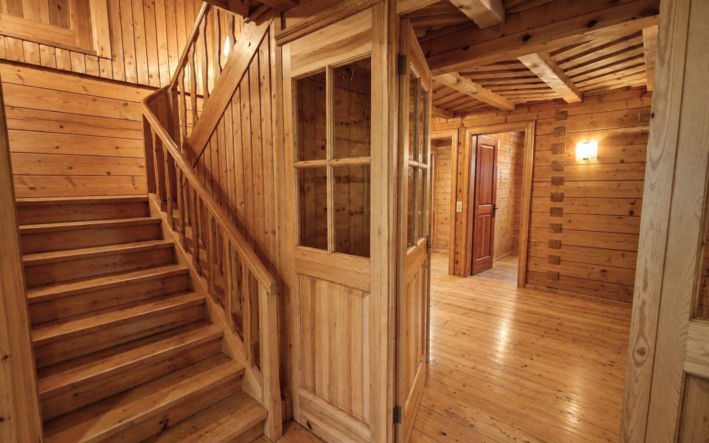 Rustikaler Holztreppenaufgang mit Holzvertäfelung und sichtbaren Deckenbalken.
