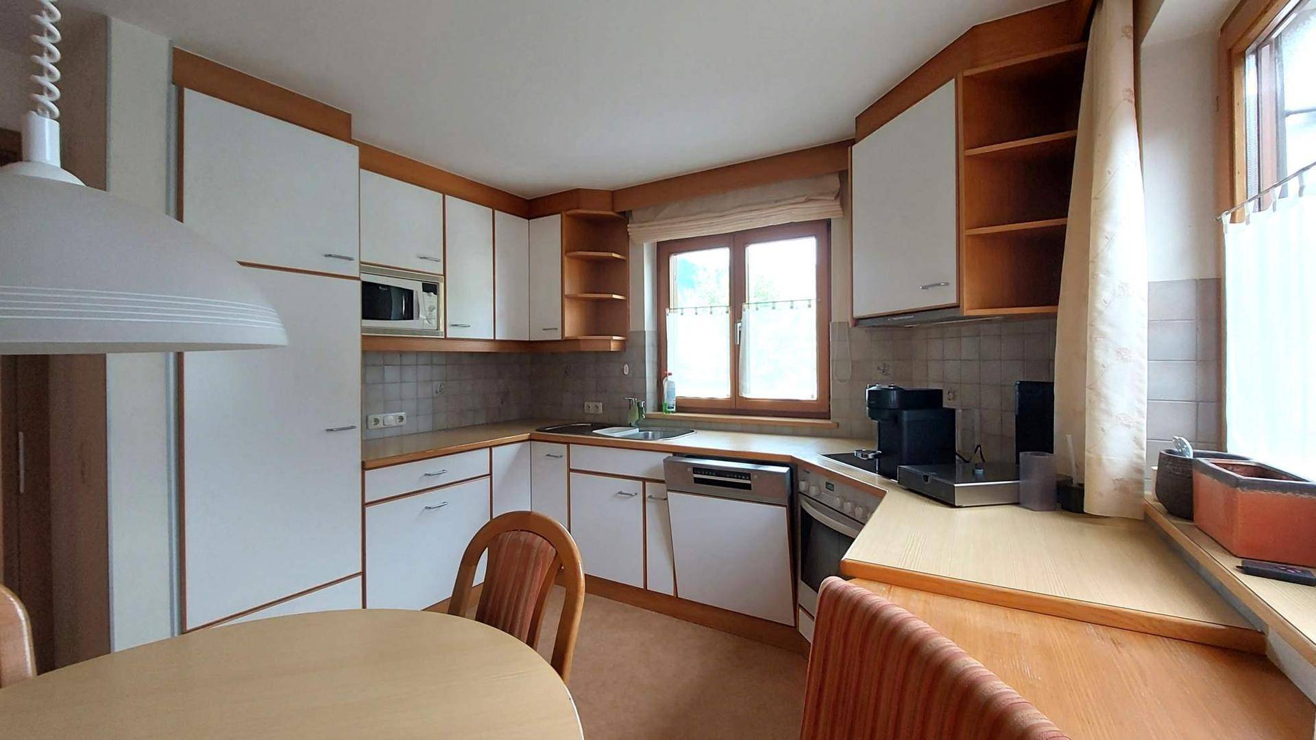 Helle Küche mit weißen Schränken, Holztheke und Essbereich, ausgestattet mit modernen Geräten.