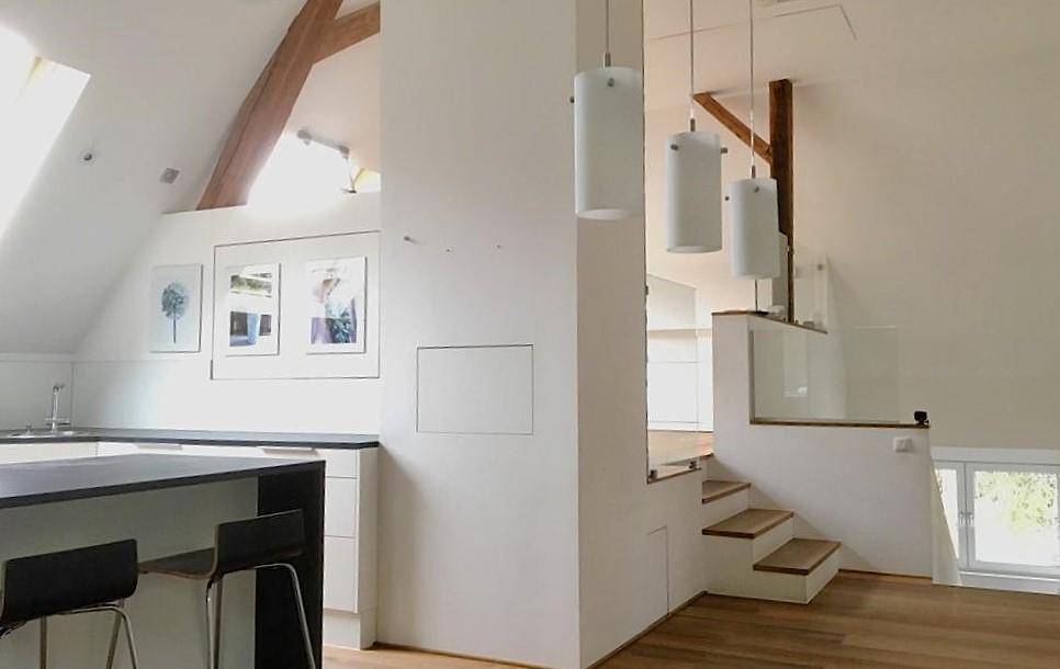 Offener Wohnbereich mit integrierter Küche, Holzbalken und Treppe zum oberen Stockwerk.