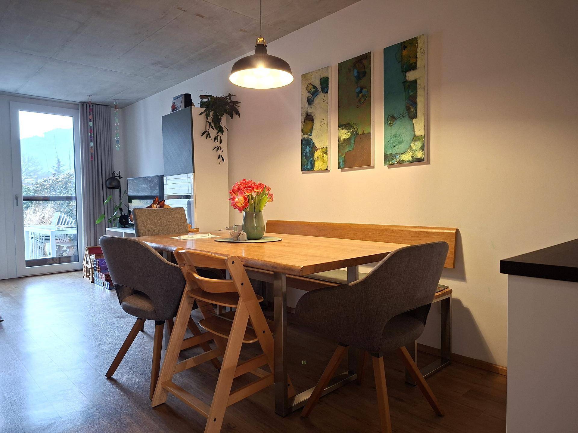 Gemütlicher Wohn-Essbereich mit Holztisch, modernen Stühlen und Zugang zum Balkon mit Bergblick.