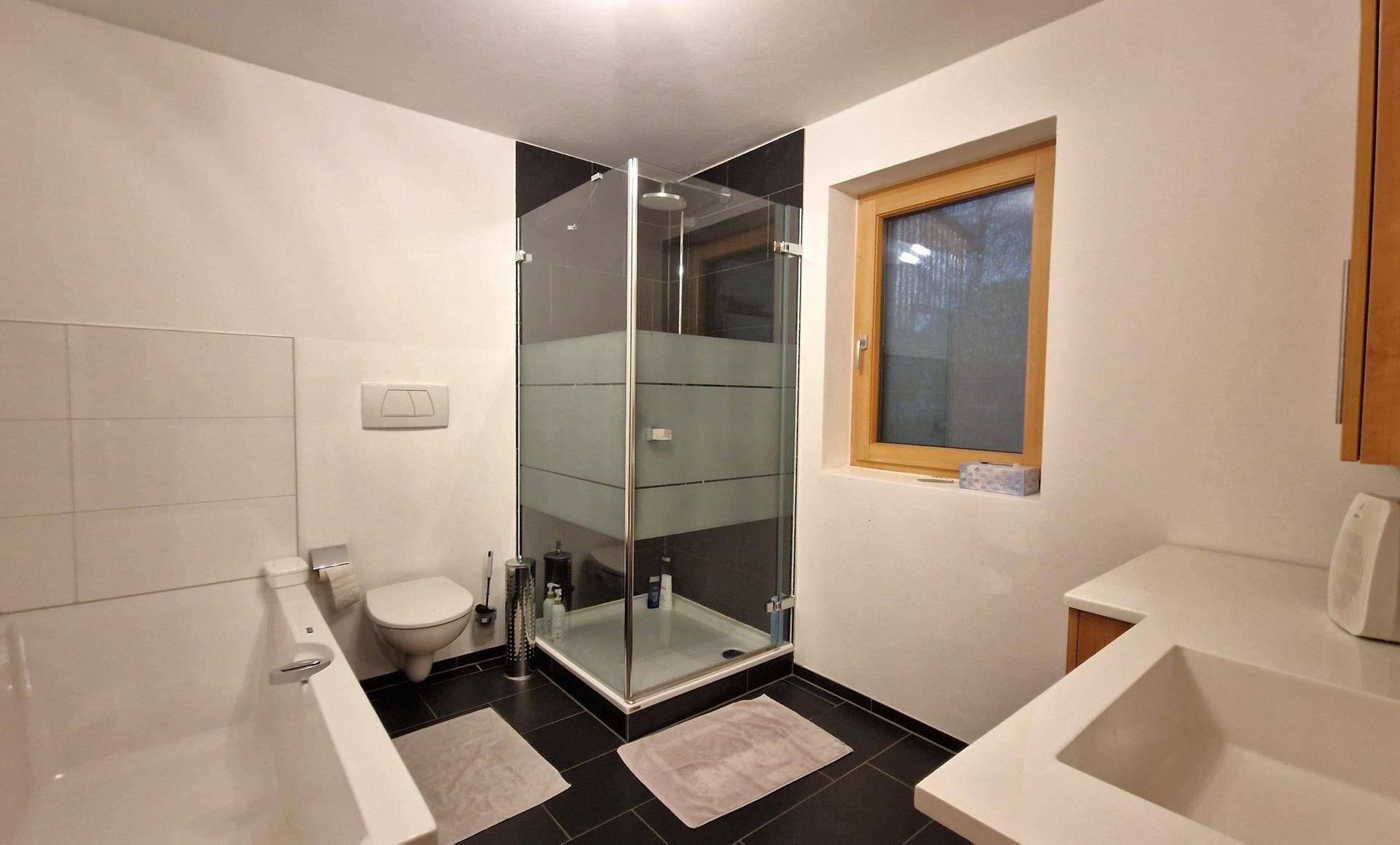 Helles Badezimmer mit Duschkabine, Badewanne und Fenster, modern gefliest.