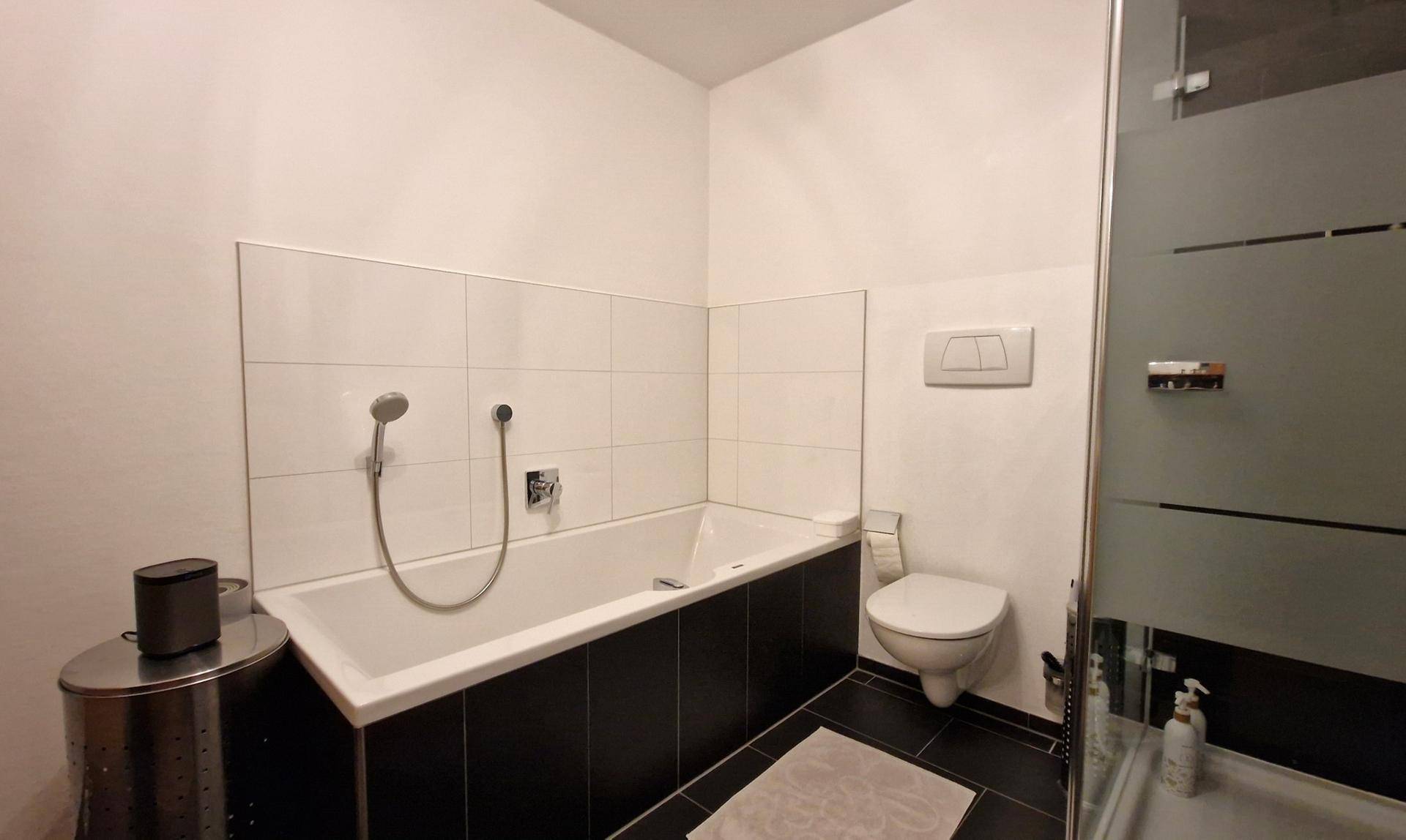 Badezimmer mit Badewanne, wandhängendem WC und dunklen Fliesen, sauber und funktional.