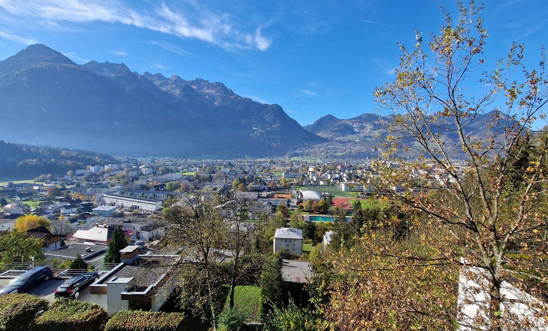Weitläufiger Ausblick auf die Stadtlandschaft und die beeindruckende Bergkulisse an einem sonnigen Tag.