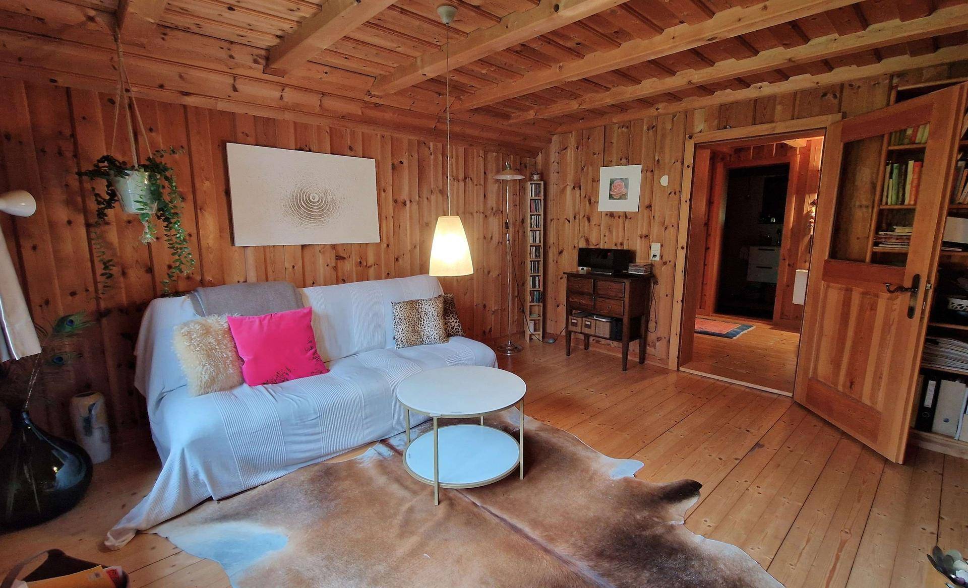 Gemütliches Wohnzimmer mit Holzboden, Holzvertäfelung, Sofa und Couchtisch.