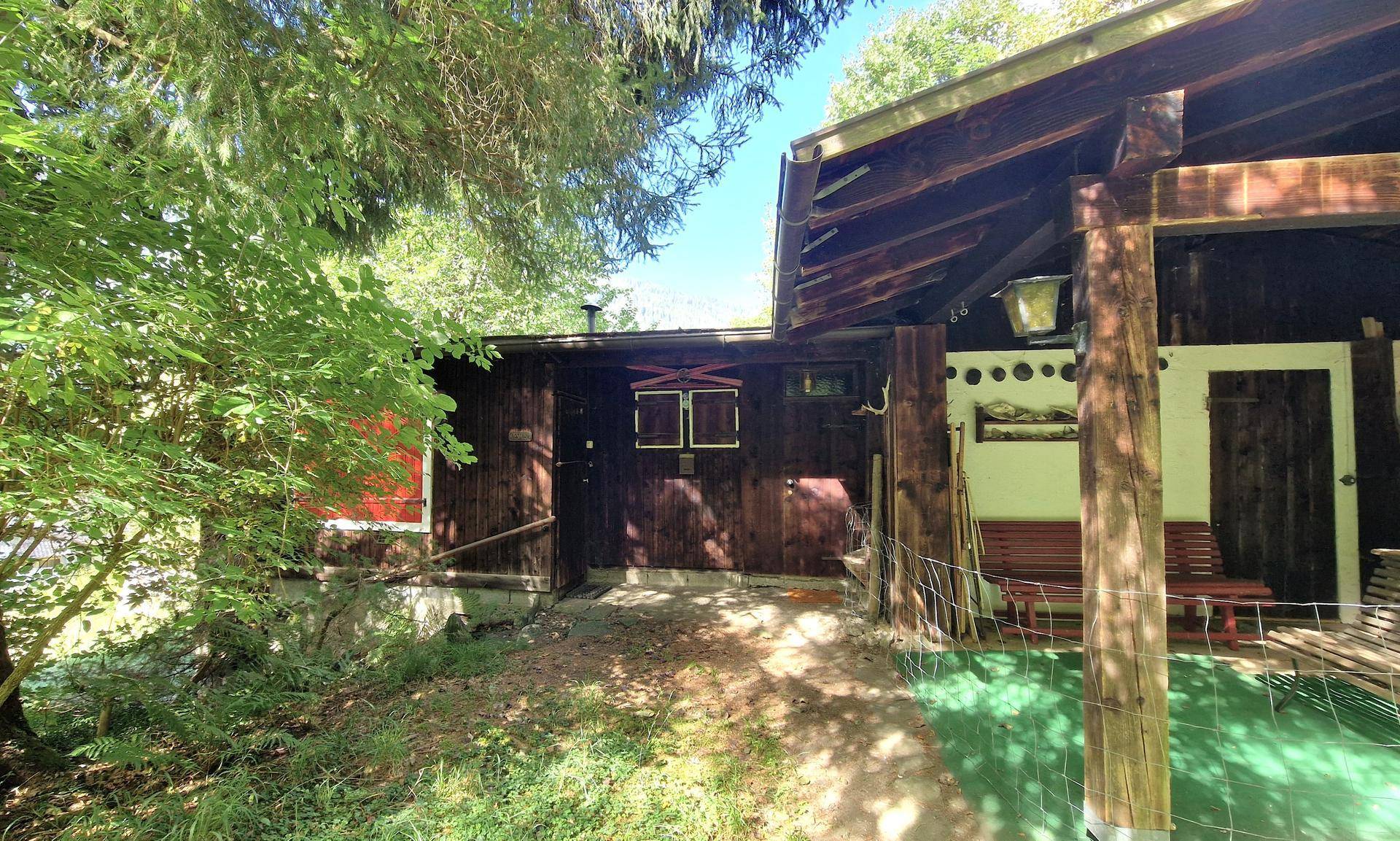 Eingangsbereich eines traditionellen Holzhauses mit überdachtem Vorbau und einer Holzbank.