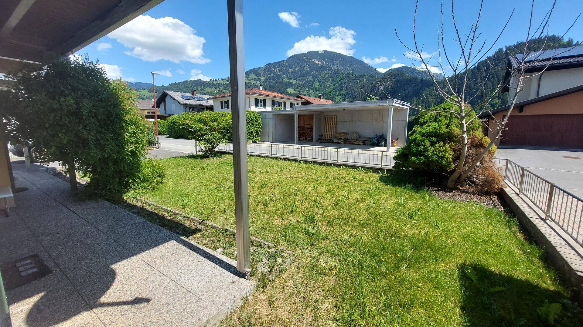 Weitläufiger Rasenbereich mit Carport im Hintergrund und malerischem Blick auf die umliegenden Berge.