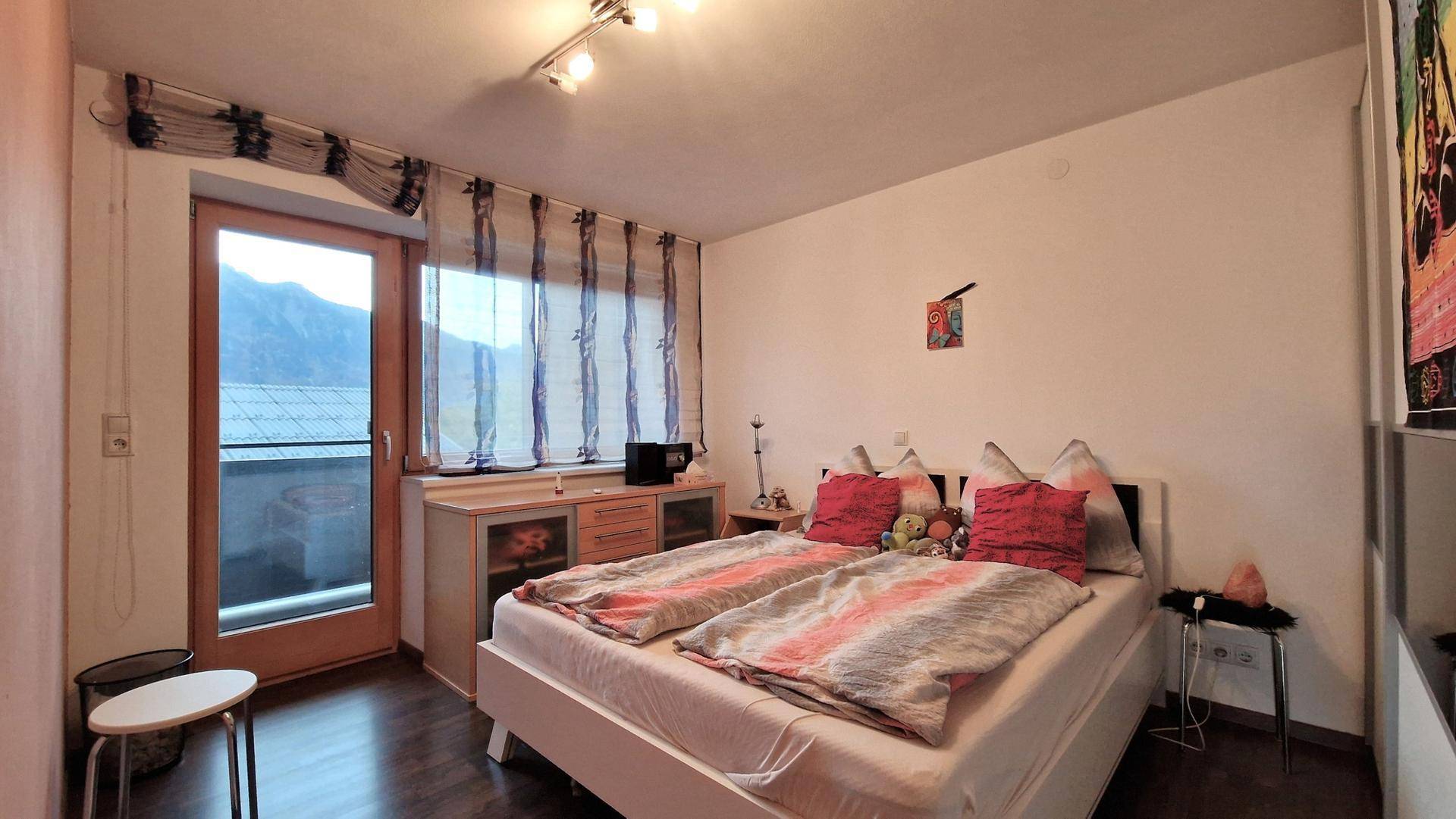 Schlafzimmer mit Doppelbett, dunklem Laminatboden und direktem Zugang zum Balkon.