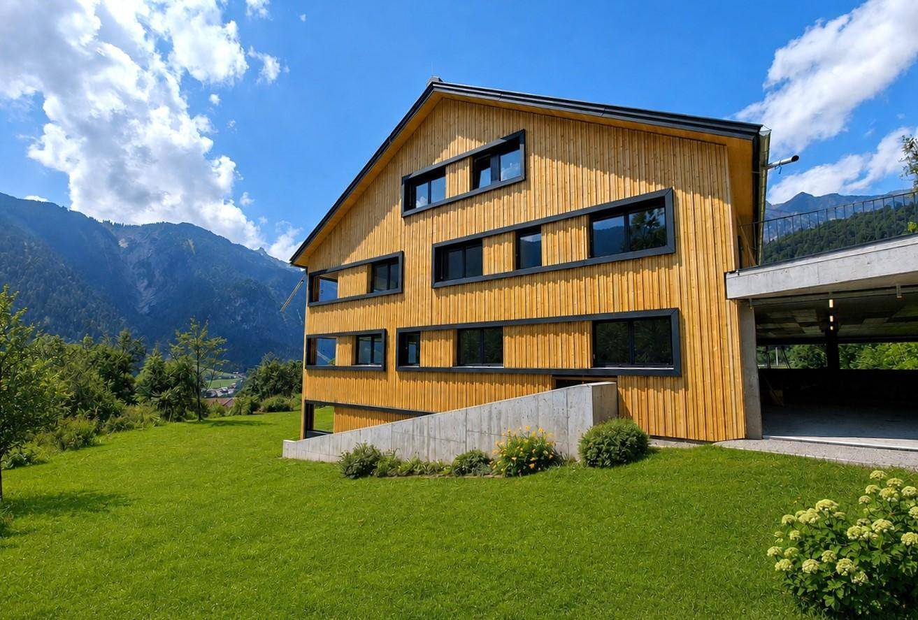 Modernes Holzgebäude mit Zufahrt zur Tiefgarage und weitem Blick auf die umliegende Berglandschaft.