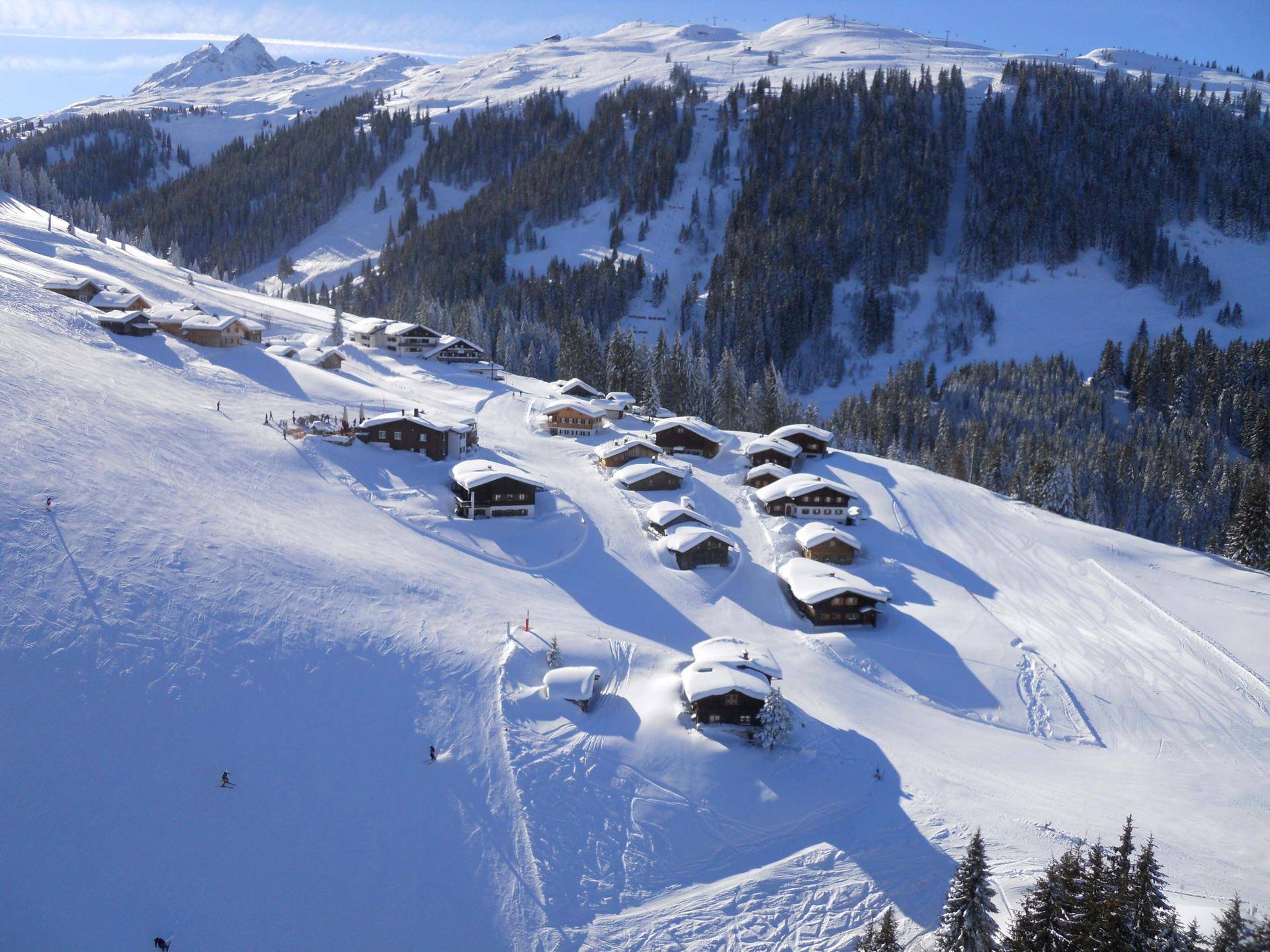 Panoramablick auf ein verschneites Bergdorf mit Skipisten und dichten Wäldern.