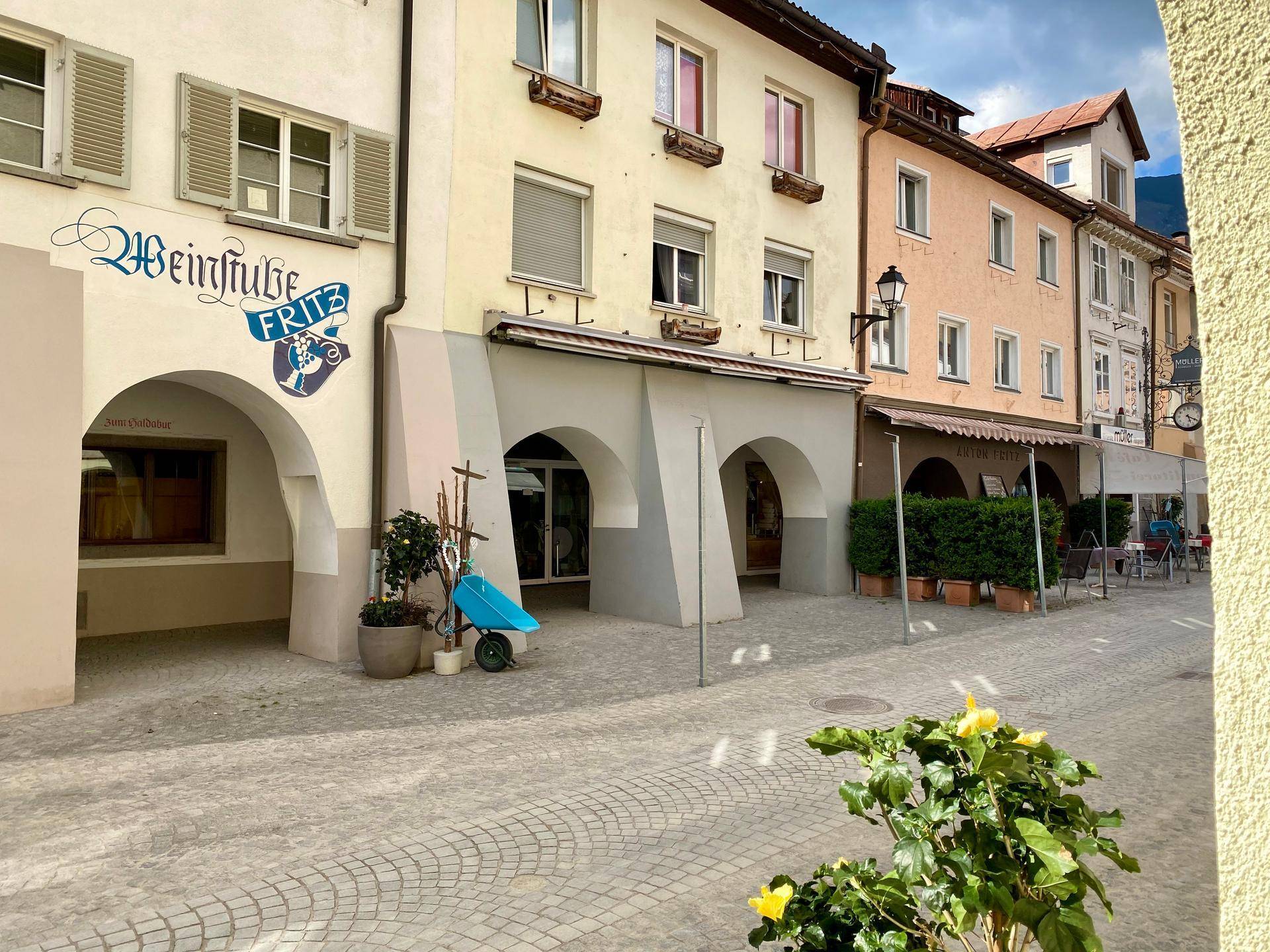 Historische Gebäude mit Arkaden und Fensterläden säumen eine gepflasterte Straße, die eine charmante Atmosphäre schafft.