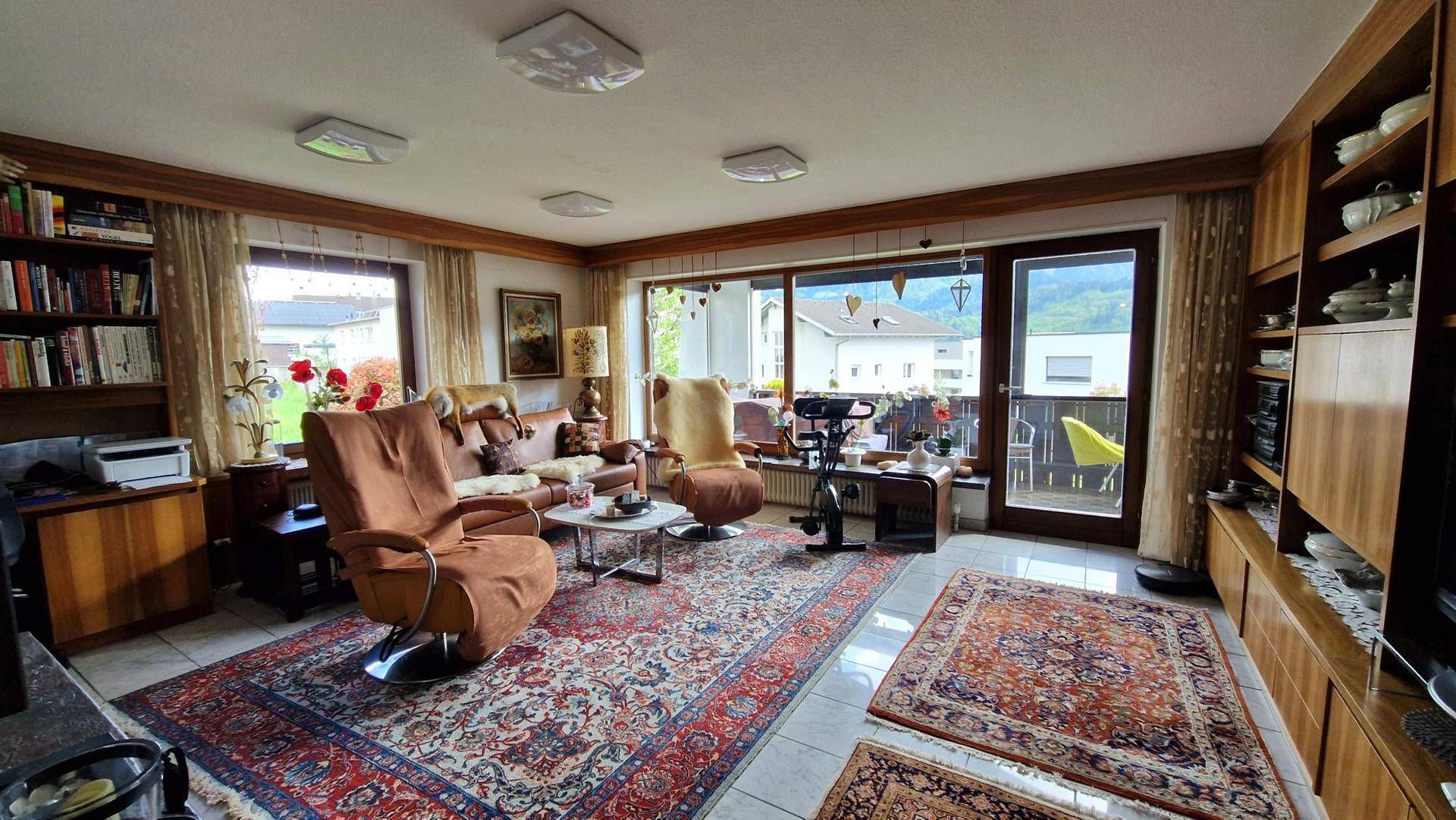 Gemütliches Wohnzimmer mit traditionellen Teppichen, großen Fenstern und Zugang zum Balkon.
