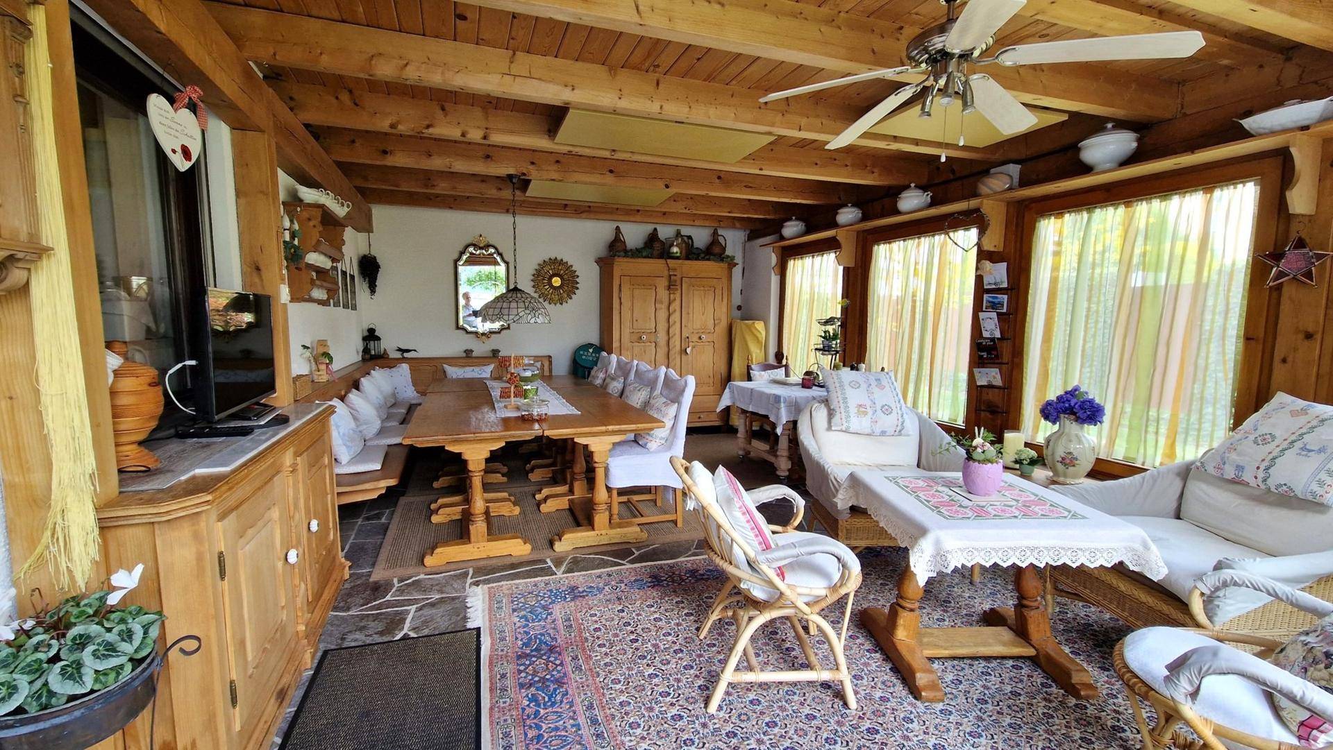 Gemütlicher Wintergarten mit Holzbalkendecke, Essbereich und Sitzgelegenheiten.