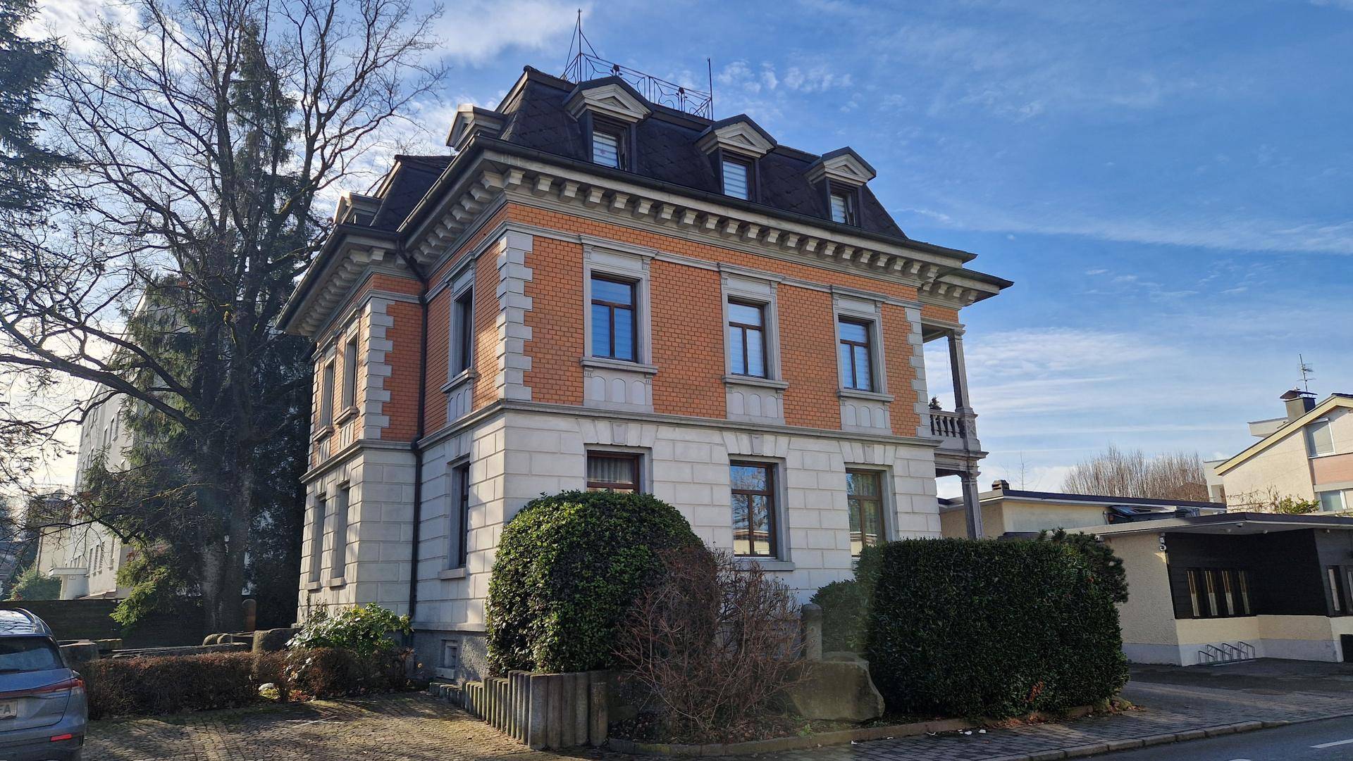 Elegantes historisches Gebäude mit Mansarddach und gepflegter Fassade an einem sonnigen Tag.