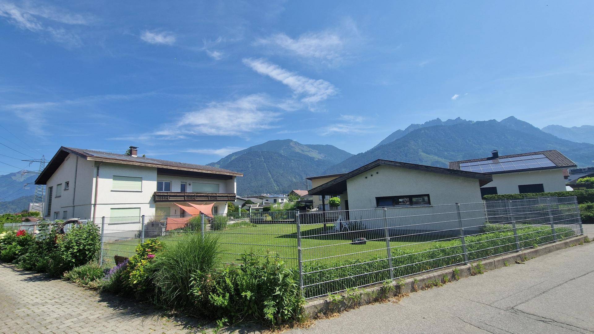 Ansicht des Hauses mit Garten und umliegender Wohnbebauung vor einer beeindruckenden Bergkulisse.