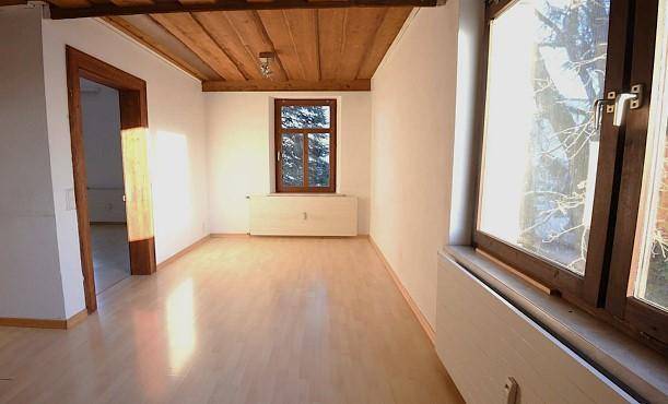 Leerer Raum mit Holzbalkendecke, Laminatboden und zwei Fenstern, bereit zur Einrichtung.