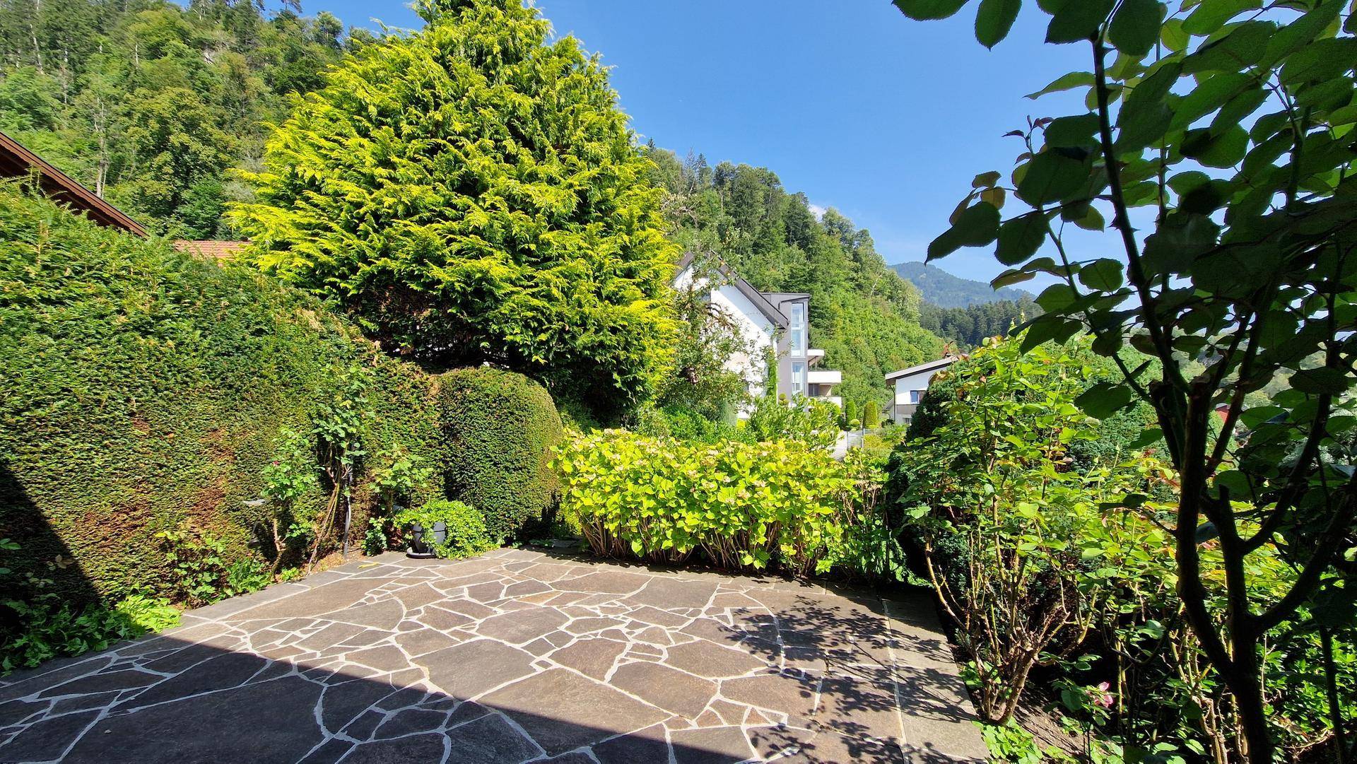 Sonniger Gartenbereich mit Natursteinpflaster und dichter Bepflanzung im Hintergrund.