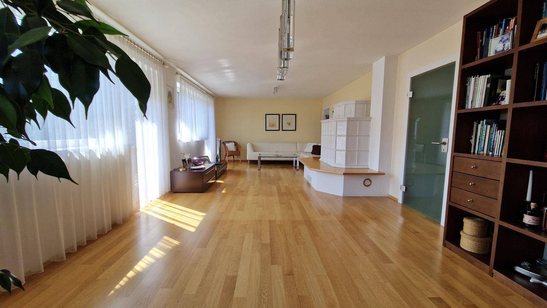 Weitläufiges Wohnzimmer mit hellem Parkettboden, Kachelofen und viel natürlichem Licht.