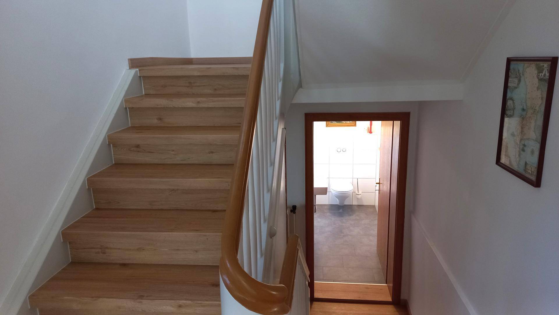 Heller Treppenaufgang mit Holzstufen und Geländer, führt zu einem Badezimmer.
