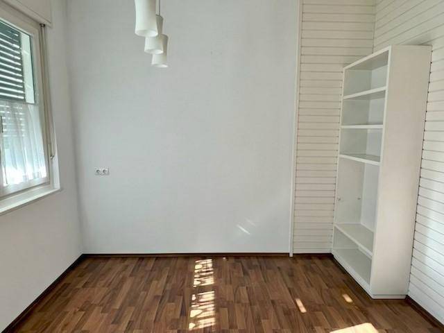 Heller Raum mit Holzboden, großem Fenster und weißem Regal.