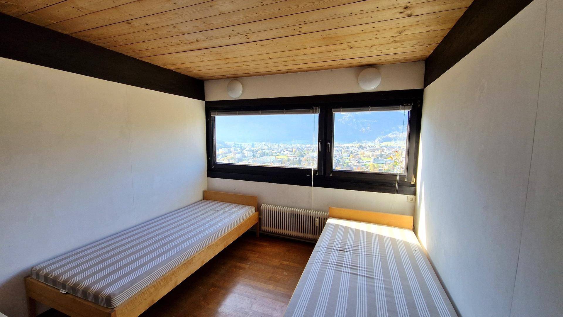 Schlafzimmer mit zwei Einzelbetten, Holzboden und weitem Blick auf die Stadt und Berge.