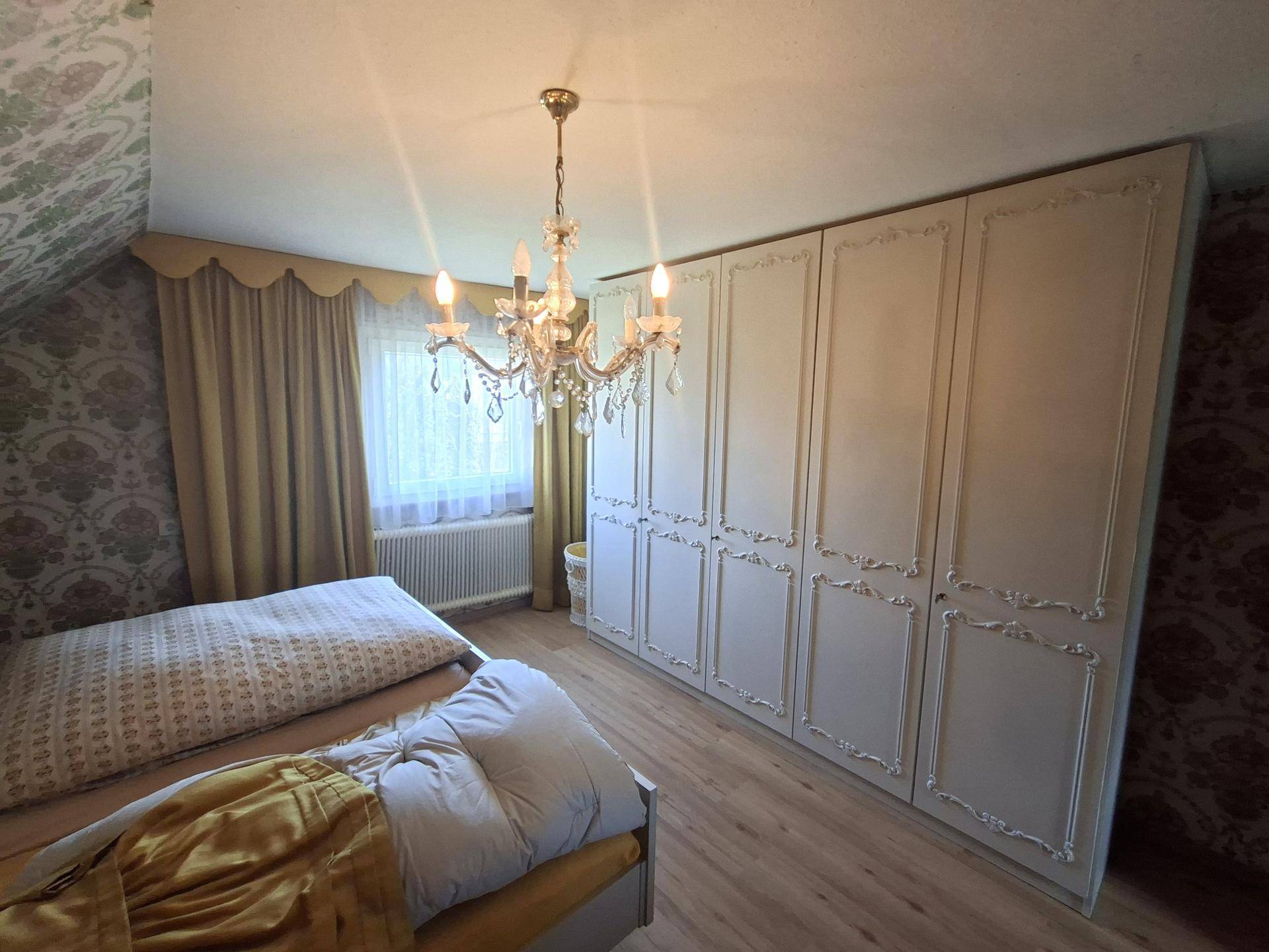 Schlafzimmer mit großem Einbauschrank, Doppelbett und Kronleuchter unter Dachschräge.