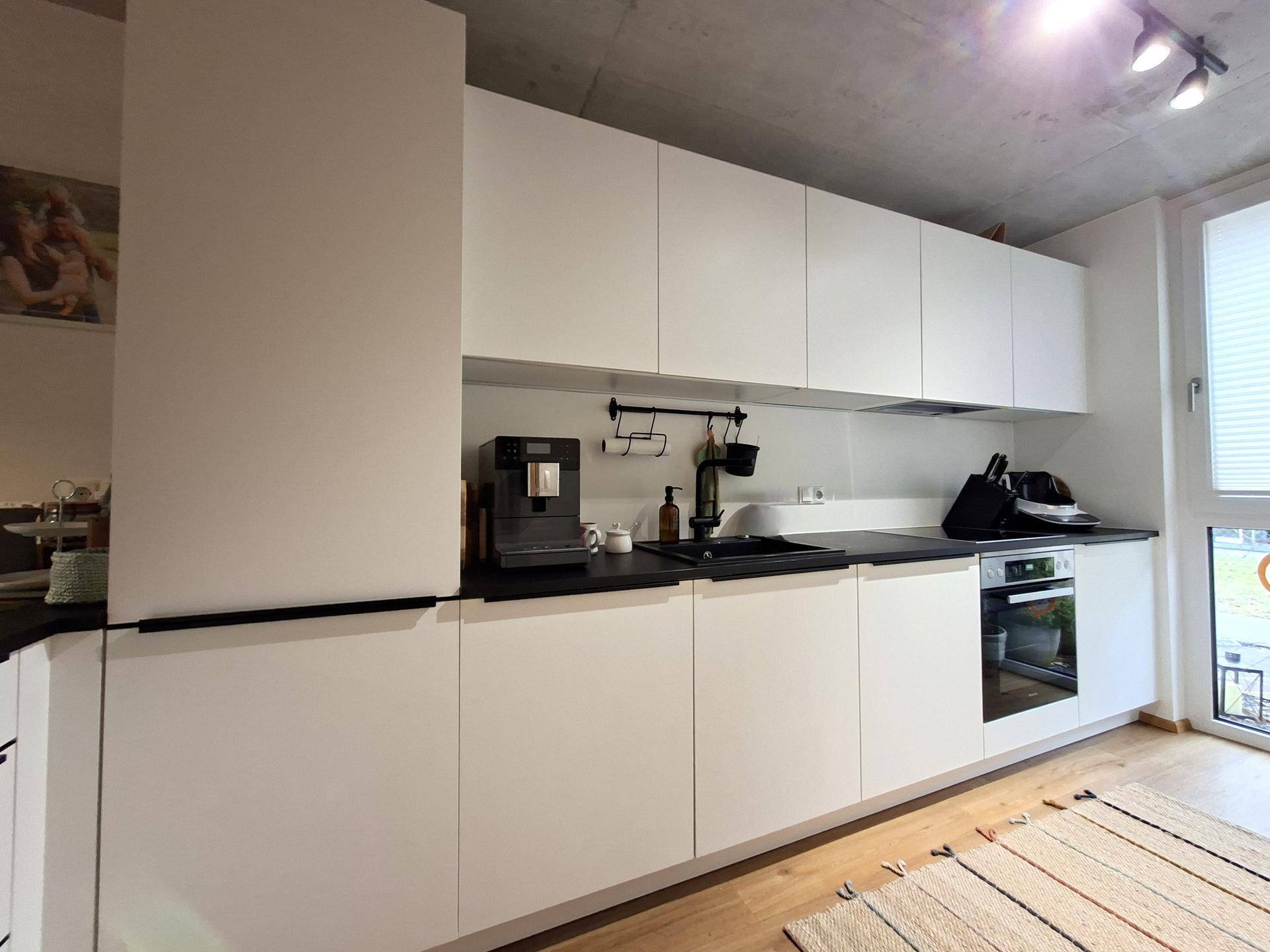Moderne weiße Küche mit schwarzen Arbeitsplatten, integrierten Geräten und Holzboden.