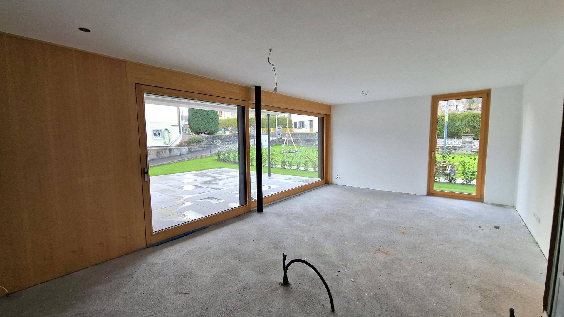 Unfertiger Innenraum mit großen Fenstern und Zugang zum Garten, bereit für den individuellen Ausbau.