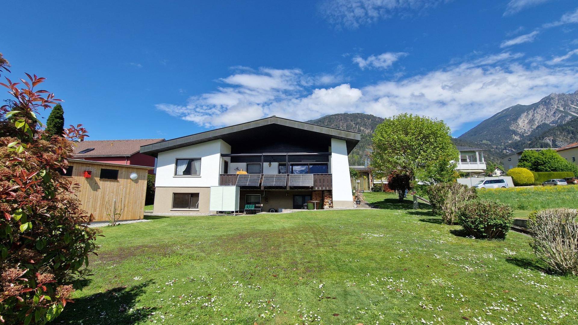 Großzügiger Garten mit Rasenfläche, Gartenhaus und weitem Blick auf die Berge.