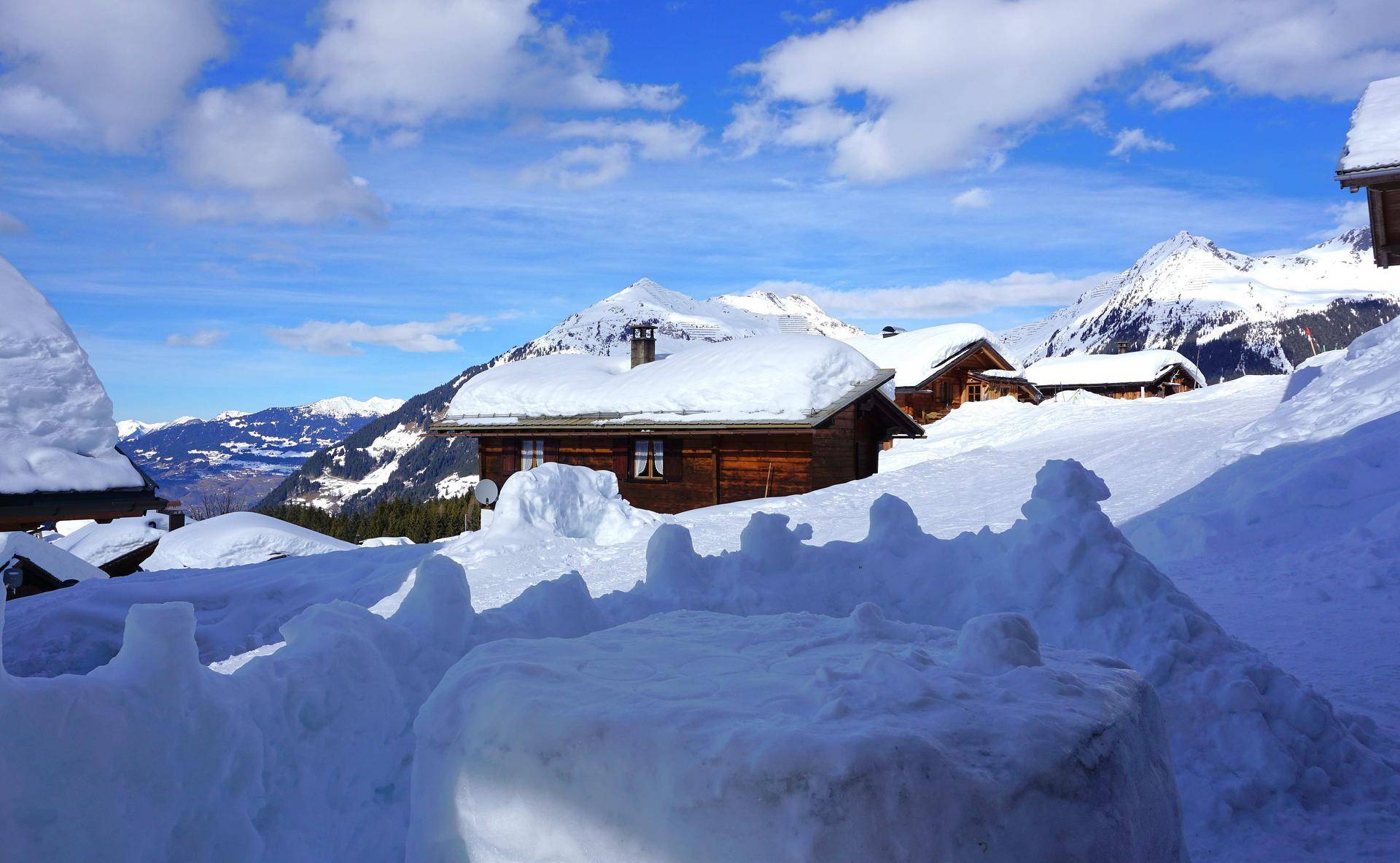 Weitläufige Schneelandschaft mit traditionellen Chalets und majestätischen Berggipfeln.