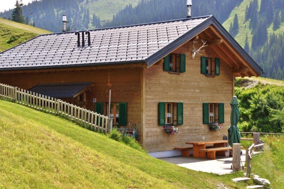 Traditionelles Holzchalet mit Terrasse und Bergblick in einer grünen Alpenlandschaft.