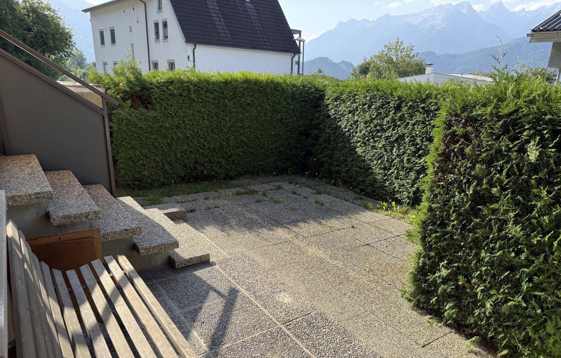 Gepflasterte Terrasse im Freien, umgeben von Hecken und mit Blick auf die Berge.