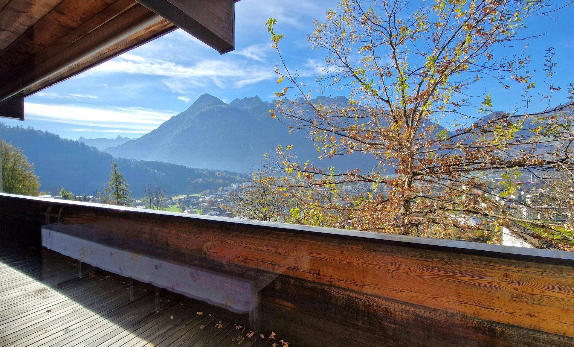 Sonniger Balkon mit Holzboden und atemberaubendem Blick auf die Berge und das Tal.
