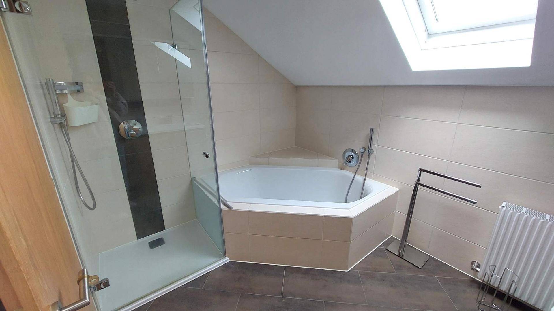 Helles Badezimmer im Dachgeschoss mit Glasdusche, Eckbadewanne und einem Dachfenster.