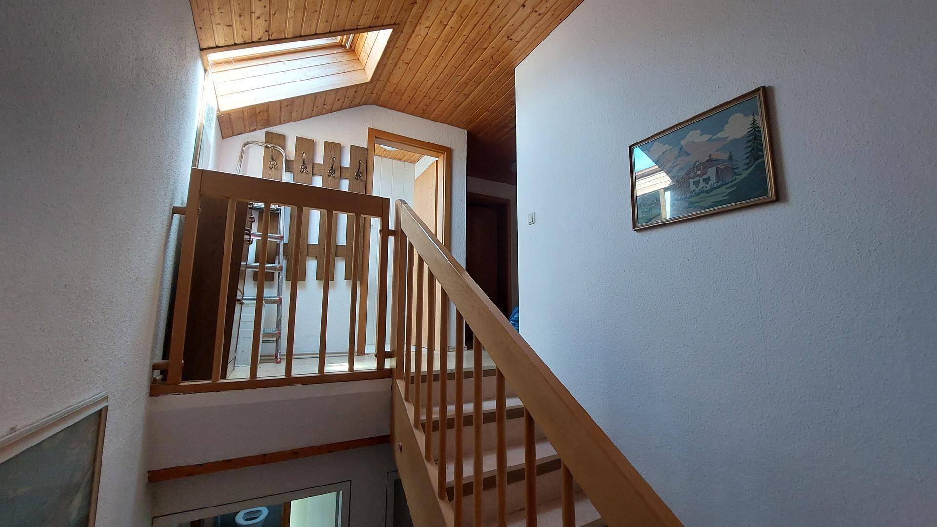 Holztreppe führt in das obere Stockwerk, beleuchtet durch ein Dachfenster, mit rustikalem Geländer.