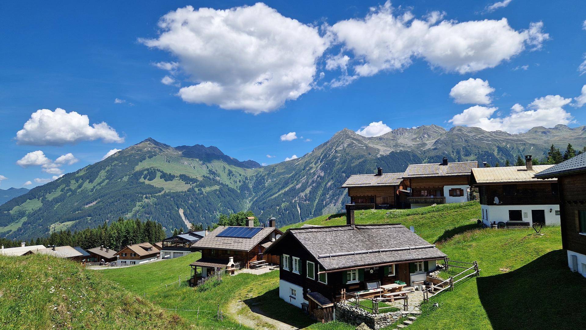 Malerisches Bergdorf mit traditionellen Häusern und weiten grünen Wiesen unter blauem Himmel.