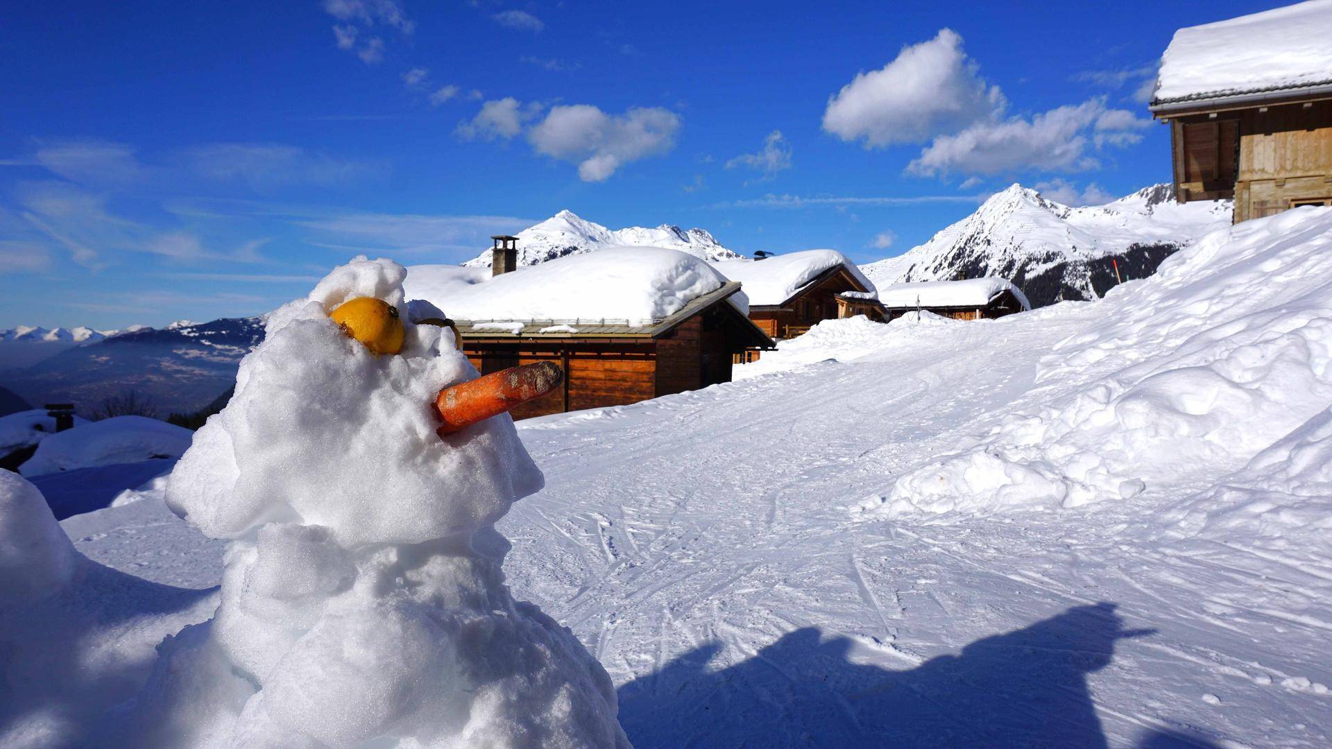 Fröhlicher Schneemann vor einer idyllischen Winterlandschaft mit verschneiten Bergen.