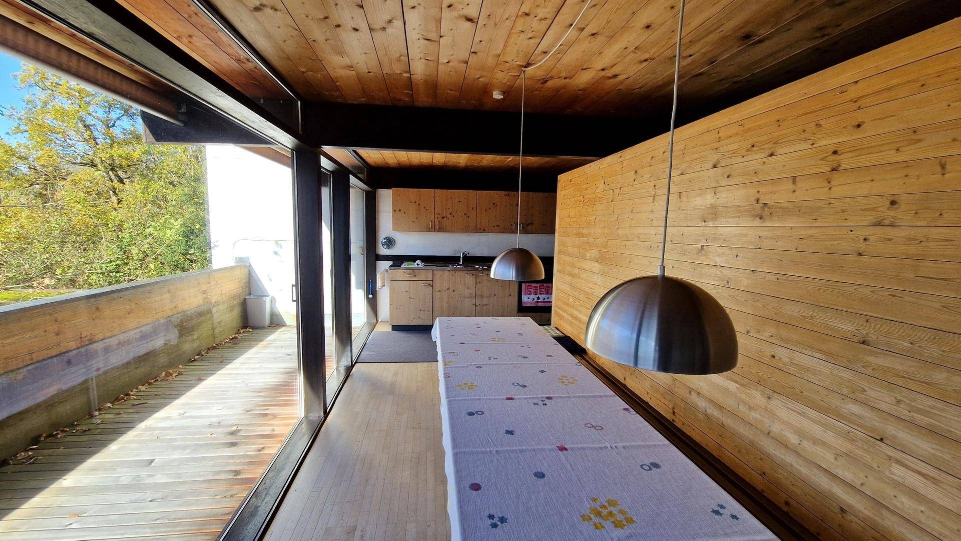 Essbereich mit Holzwänden und Decke, großen Fenstern und Blick ins Grüne.