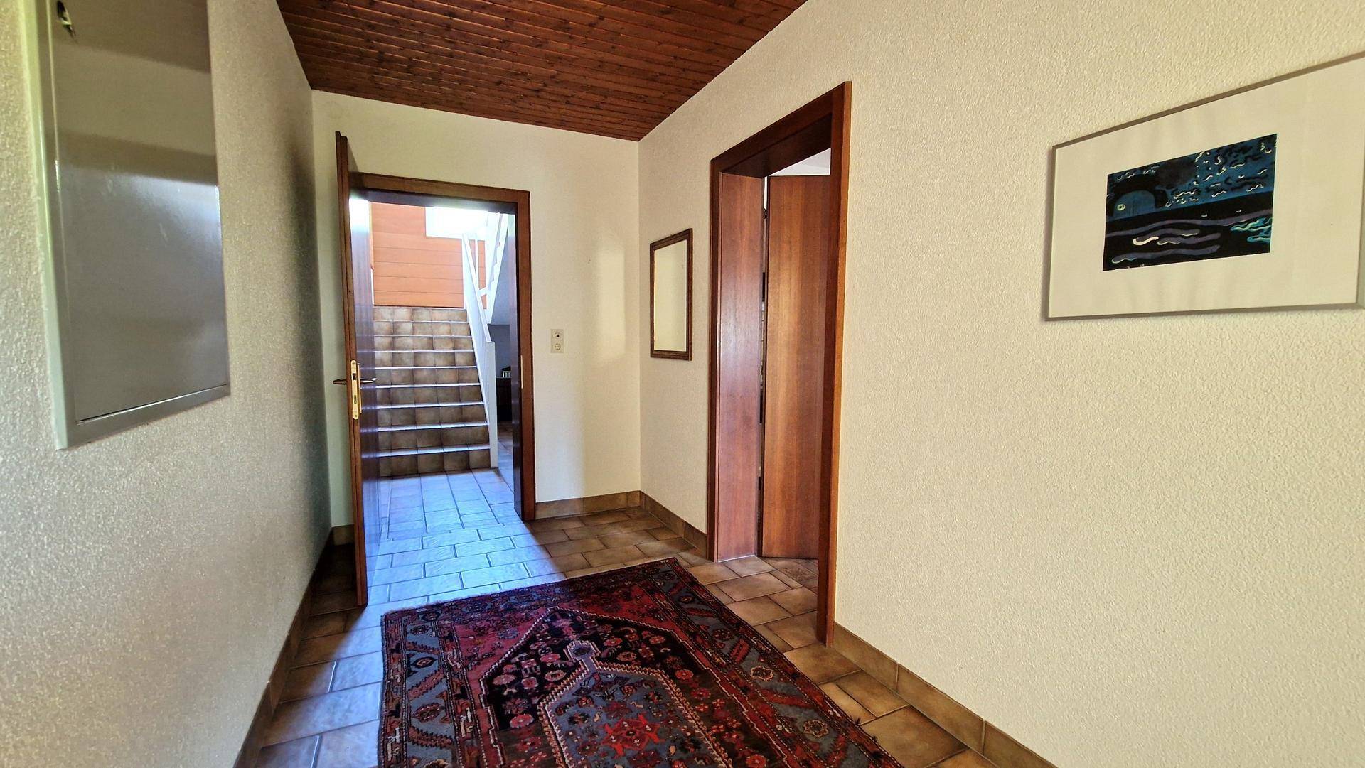 Heller Flur mit Fliesenboden, Holzdecke und Zugang zu weiteren Räumen sowie einer Treppe.